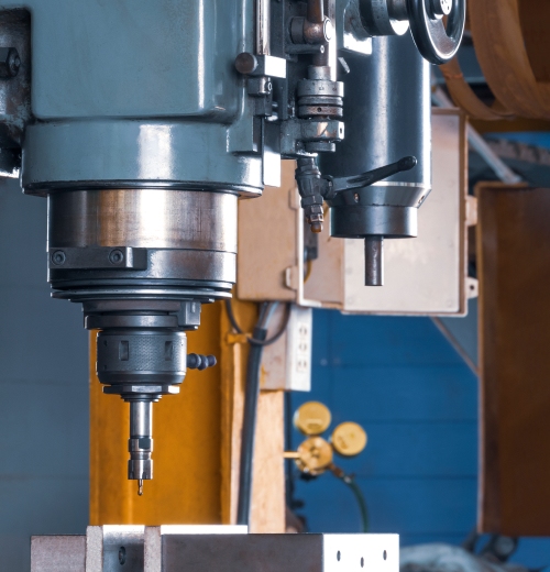 Industrial milling machine spindle with cutting tool in a blue-gray workshop setup, metal components and controls visible nearby.